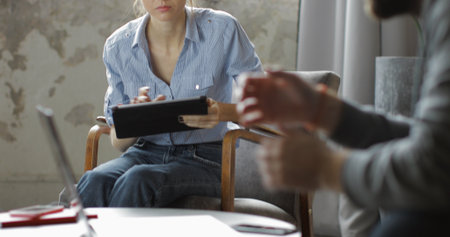Two creative people talking in home office. Young woman using digital tablet computer. Freelance...