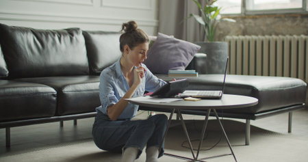 Girl sitting on floor and using digital tablet computer in home indoors, making notes. Young woman shopping online. Freelance female model working out of office.の写真素材