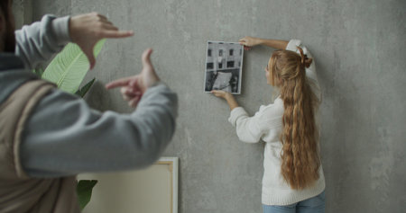 Young woman hanging picture on wall while young man lookingの写真素材
