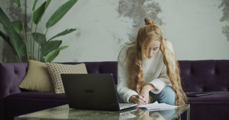 Girl sitting on sofa and using pc computer laptop in home indoors. Young woman using notebook , making notes. Freelance female model working out of office.の写真素材