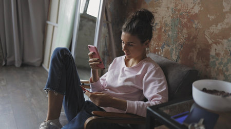 Happy young woman relaxing at home sit on sofa holding digital tablet enjoying surfing internet...