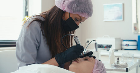 Microblading eyebrows work flow in a beauty salon. Woman having her eye brows tinted. Semi-permanent makeup for eyebrowsの写真素材