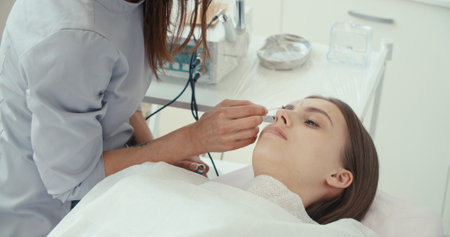 Relaxed female client lying on white couch during spa procedure . Hands of qualified therapist. Concept of body care and treatment, semi-permanent make-upの写真素材