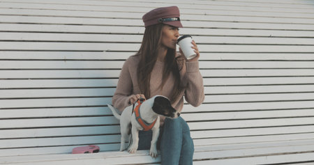 Pretty caucasian woman with dog jack russell terrier sitting on bench and drinking coffee. Cute little puppyの写真素材
