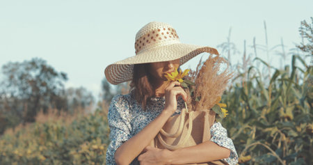 beautiful sweet sexy girl in a blue dress and hat walking on a field of sunflowers , cheerful woman sniffing flowers, countryside style, lifestyleの写真素材