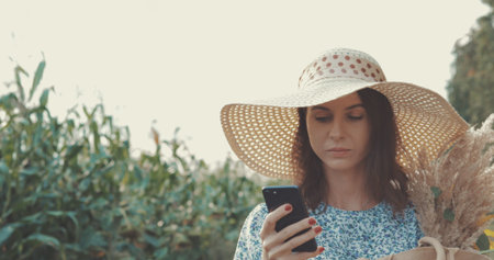 Woman takes selfie on smartphone at sunflower field. Sweet sexy girl in a blue dress and hat walks...