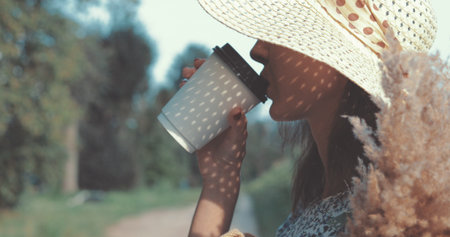 beautiful sweet sexy girl in a blue dress and hat walking on a field of sunflowers , cheerful woman drinks hot coffee from paper glass, lifestyleの写真素材