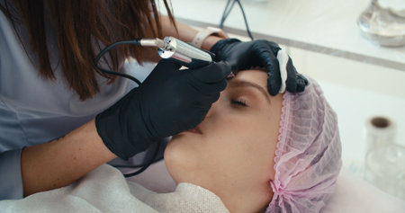 Microblading eyebrows work flow in a beauty salon. Woman having her eye brows tinted. Semi-permanent makeup for eyebrowsの写真素材