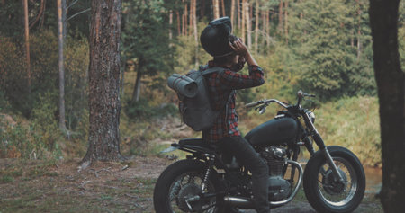Hiker camping in forest. Guy biker with backpacker on his back sits on motorcycle in forest by river. Freedom lifestyle sceneの写真素材