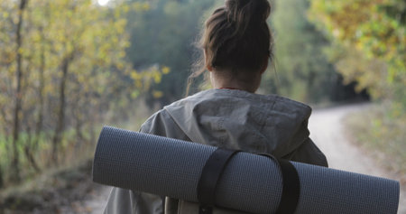 Active healthy female hipster model hiking along forest mountain road. Caucasian girl rest outdoors . Woman tourist walking in fall park at sunny autumn day. Back viewの写真素材