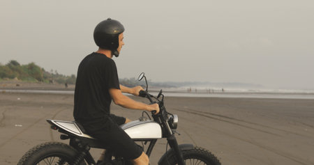 Motorcyclist driving his motorbike on ocean beach during sunset
