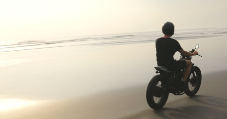 Motorcyclist driving his motorbike on ocean beach during sunsetの写真素材
