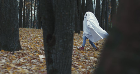 Little girl in a costume ghost with orange pumpkin in autumn park or forest. Halloween celebration...
