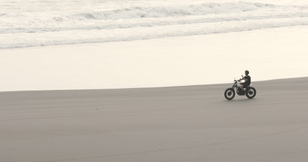 Motorcyclist driving his motorbike on ocean beach during sunsetの写真素材