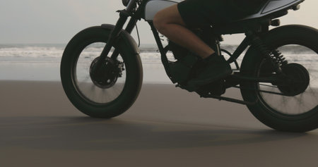 Motorcyclist driving his motorbike on ocean beach during sunsetの写真素材
