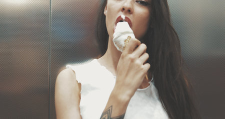 Closeup of a young girl in a white T-shirt holds a waffle cone with melt ice creamの写真素材