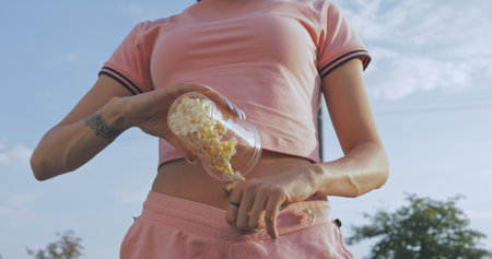 Funny girl pours popcorn from glass in pink shortsの写真素材