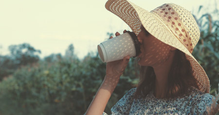 beautiful sweet sexy girl in a blue dress and hat walking on a field of sunflowers , cheerful woman drinks hot coffee from paper glass, lifestyleの写真素材