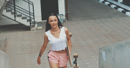 Young girl walks up stairs with skateboard. Sporty pretty woman with longboard looking to camera.の写真素材