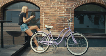 Young modern woman riding bicycle in city. Girl texting reading messages on smartphoneの写真素材