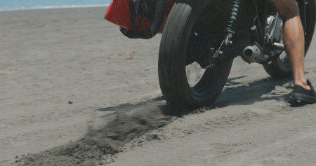 Handsome man biker surfer driving his black motorbike cafe racer with red surfboard shortboard on...