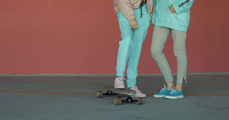 Smiling woman standing on a longboard while her friend is pushing her behind and running in car parking. Enjoying life. Urban city lifestyleの写真素材