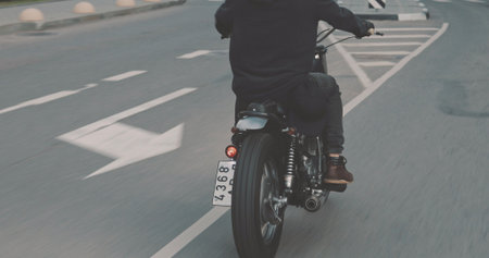 Motorcyclist drives on a motorcycle on the road in the city. Biker rides a vintage custom motorbike from 1970s . Urban lifestyle scene. Back viewの写真素材