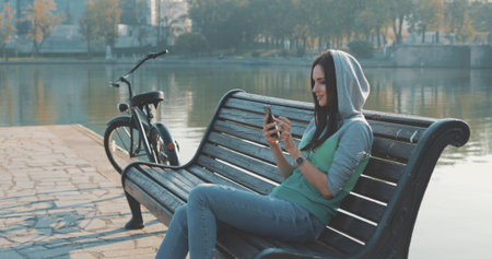 Brunette hipster woman wearing in hoodie selfie in park . Caucasian girl work with mobile phone ,...