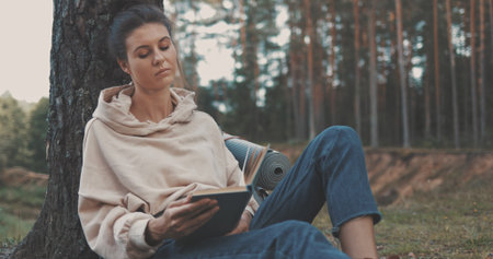 attractive young woman reading book on nature near riverの写真素材
