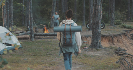 Young woman hiking in forest. Hiker camping in woods. Tourist walking along the river. Girl greeting friends sitting by campfire in campの写真素材