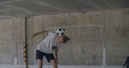 Teenager girl football soccer player doing ball tricks inside empty covered parking garage. Urban city lifestyle outdoors concepte. 4K UHD slow motion RAW graded footageの写真素材