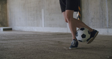 Teenager girl football soccer player doing ball tricks inside empty covered parking garage. Urban...