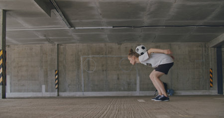 Teenager girl football soccer player doing ball tricks inside empty covered parking garage. Urban city lifestyle outdoors concepte. 4K UHD slow motion RAW graded footageの写真素材