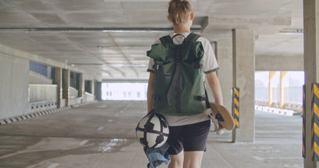 Teenager girl football soccer player walking inside empty covered parking garage. Skater holding...