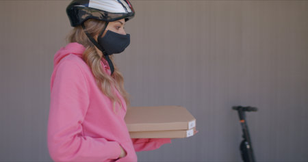 Delivery man waiting for customer at entrance door of modern house. Female courier wearing in...