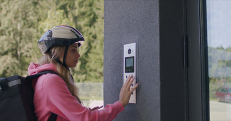 Female courier with isothermal food case box arrives on a electric scooter to the entrance to the...