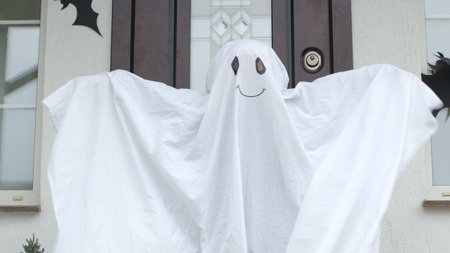 A girl in a ghost costume stands on the porch of the house with pumpkins decorated for Halloweenの写真素材