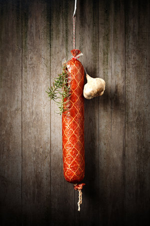 Salami Sausage hanged to dry with Garlic and Rosemary against an old rustic wooden wallの写真素材
