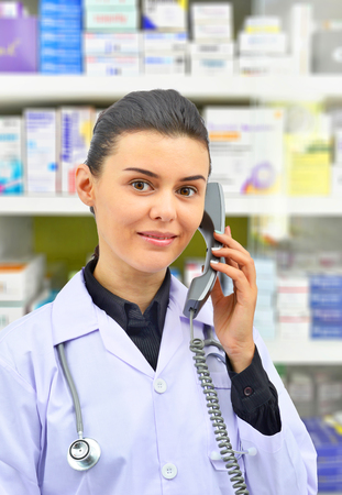 Beautiful young doctor or pharmacist talking to someone on phone on pharmacy backgroundの写真素材