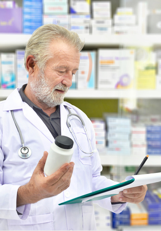 Senior doctor looking medicine bottle and patient chart on medicine shelves background,Pharmacist filling prescription in pharmacy drugstore.の写真素材