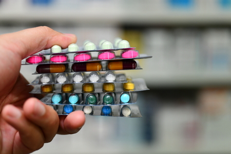Pharmacist holding medicine box and capsule pack in pharmacy drugstore.