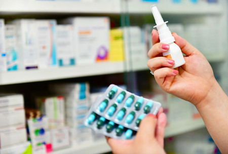 Close up shot pharmacist holding nasal spray medicine and capsule pack at the drugstore.Seasonal health issuesのeditorial素材