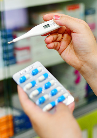 Hand holding digital thermometer capsule pack at the pharmacy on shelvesの写真素材