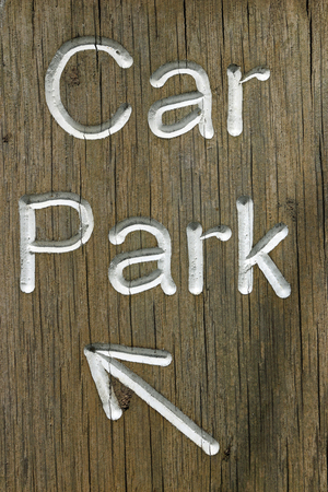 Rustic car park directional sign routed into well grained wood and with white letters spelling the words car park and a white arrow pointing to the top left.の写真素材