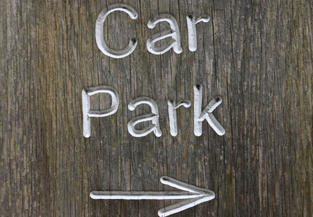 Rustic car park directional sign routed into well grained wood and with white letters spelling the words car park and a white arrow pointing to the right.の写真素材