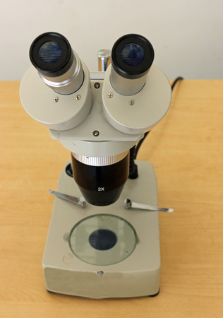 Binocular microscope with stand used for college teaching or laboratory work on a light brown table.