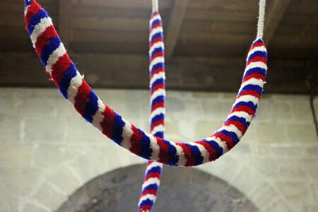 Two red, white and blue coloured bell ropes hanging down from the bell tower of a church with a...