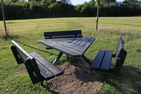 Triangular black recycled plastic picnic table with a metal frame in a park with a grass meadow and...