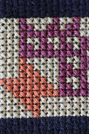 White, red and purple cross stitch embroidery on black aida in close up.の写真素材