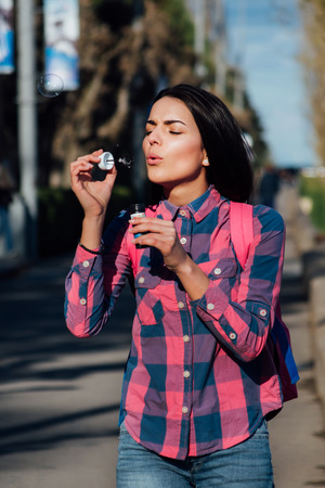 pretty woman in jeans and a jacket inflates soap bubbles on quayの写真素材